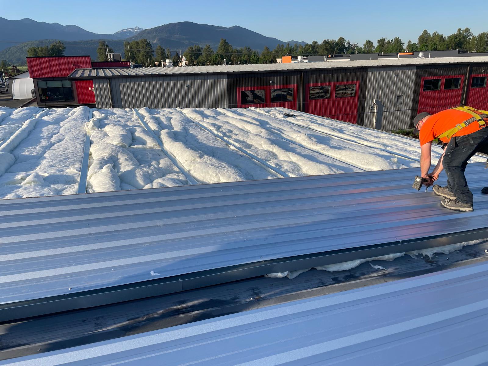 EDAPT team installing roof metal with Fraser Valley mountains in background